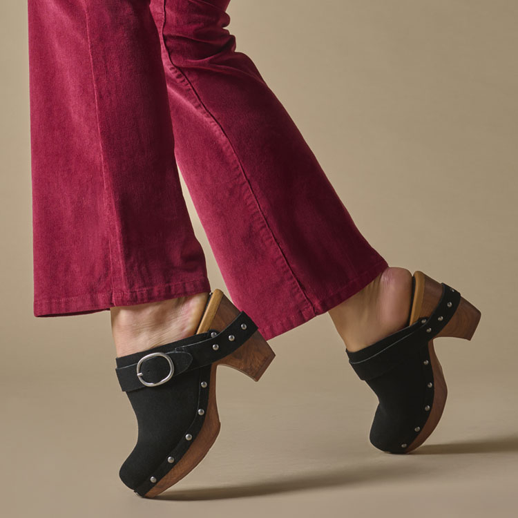 A woman wearing the Gemini heeled clog in black suede.